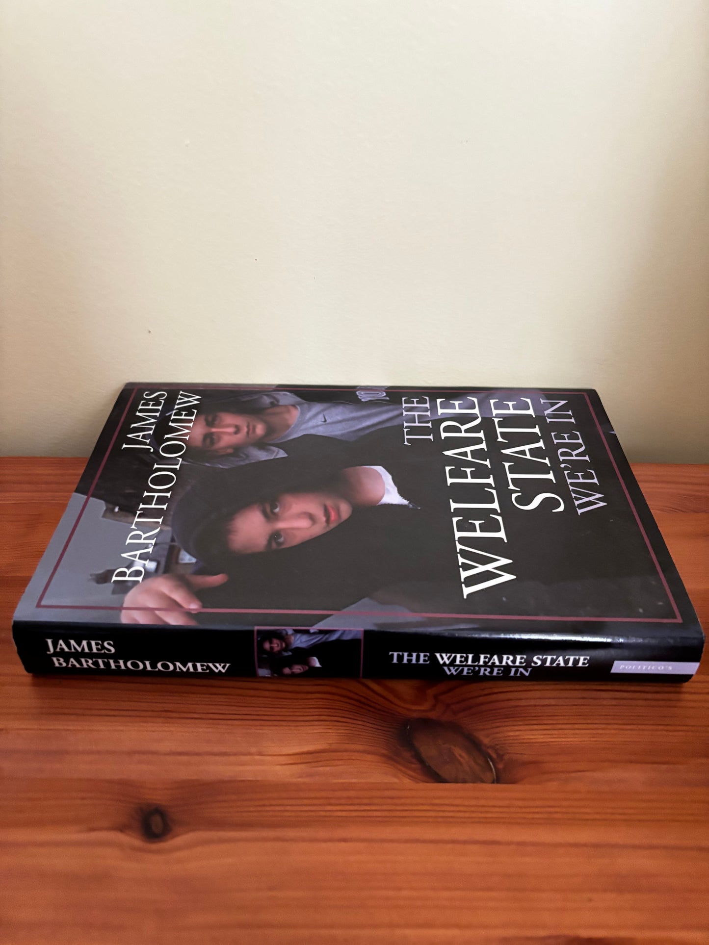 The Welfare State We're in Paperback – 15 May 2006 by James Bartholomew on a wooden surface, showcasing its cover design.