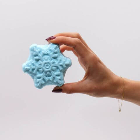 Hand holding a snowflake-shaped bath bomb from the Break the Ice Christmas Bath Bomb Gift Pack for festive relaxation.