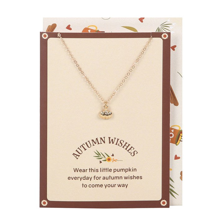Gold-toned pumpkin pendant necklace displayed on a cream autumn greeting card with envelope.