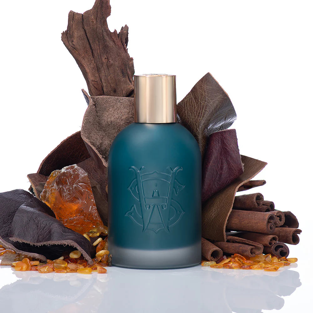 Saltworks Eclipse fragrance bottle with teal frosted glass and gold cap, surrounded by cinnamon sticks and amber.