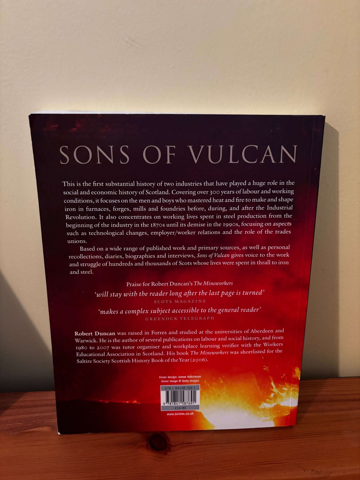 Back cover of a book titled 'Sons of Vulcan' on a wooden surface.