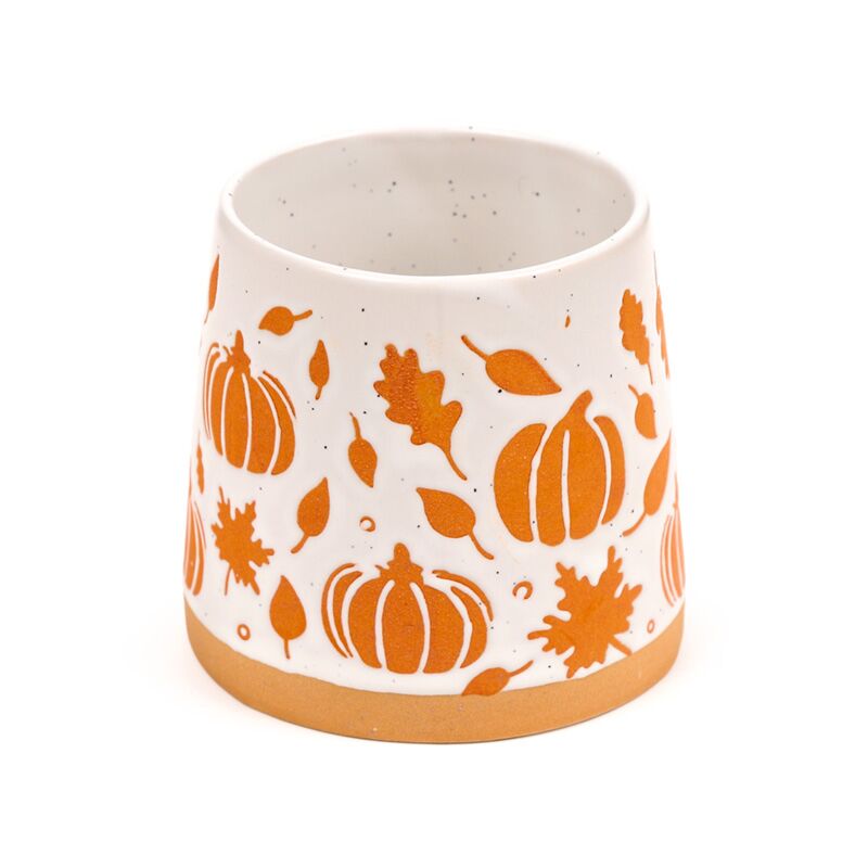 Stoneware mug featuring orange pumpkin and leaf motif on white glaze with a brown base.