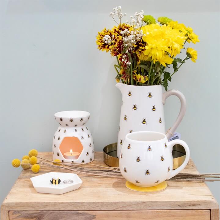 All Over Bee Print Oil Burner ceramic fragrance warmer with bee-print pieces on a wooden table and yellow flowers