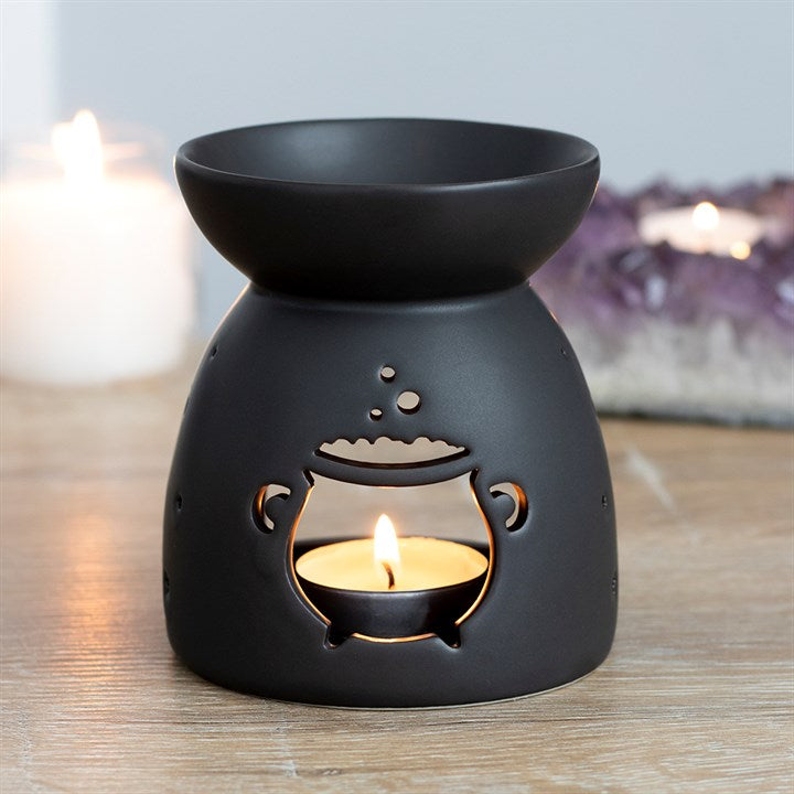 Black ceramic oil burner with cutout cauldron design and a matte finish, lit tealight inside.