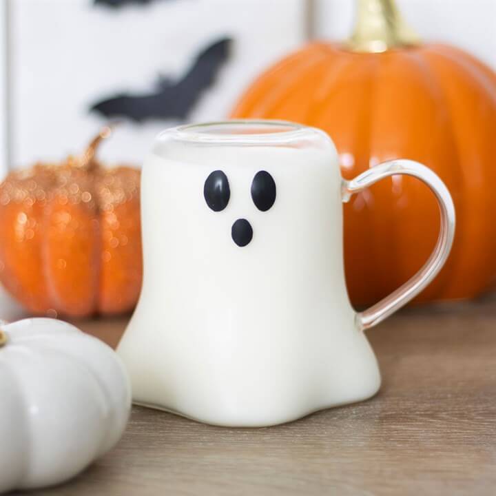 Ghost Shaped Glass Mug featuring a cute ghost face; white glass with a clear handle, autumn pumpkins in the background.