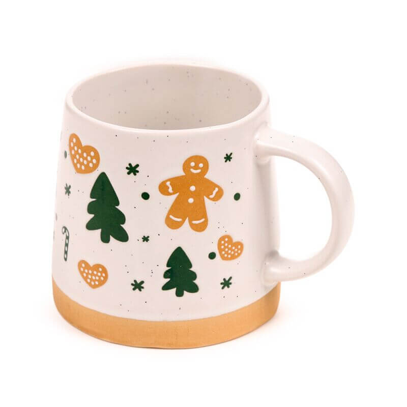 Stoneware mug featuring a gingerbread man, green trees, orange hearts, speckled glaze and tan base.