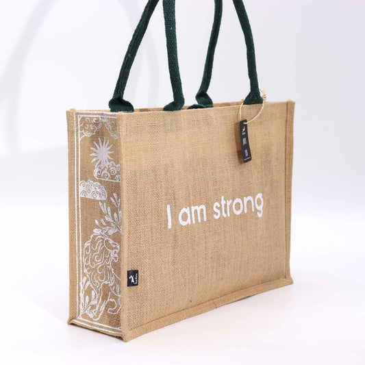 Beige jute tote with dark green handles, white I am strong text on the front and a decorative white panel along the left edge.