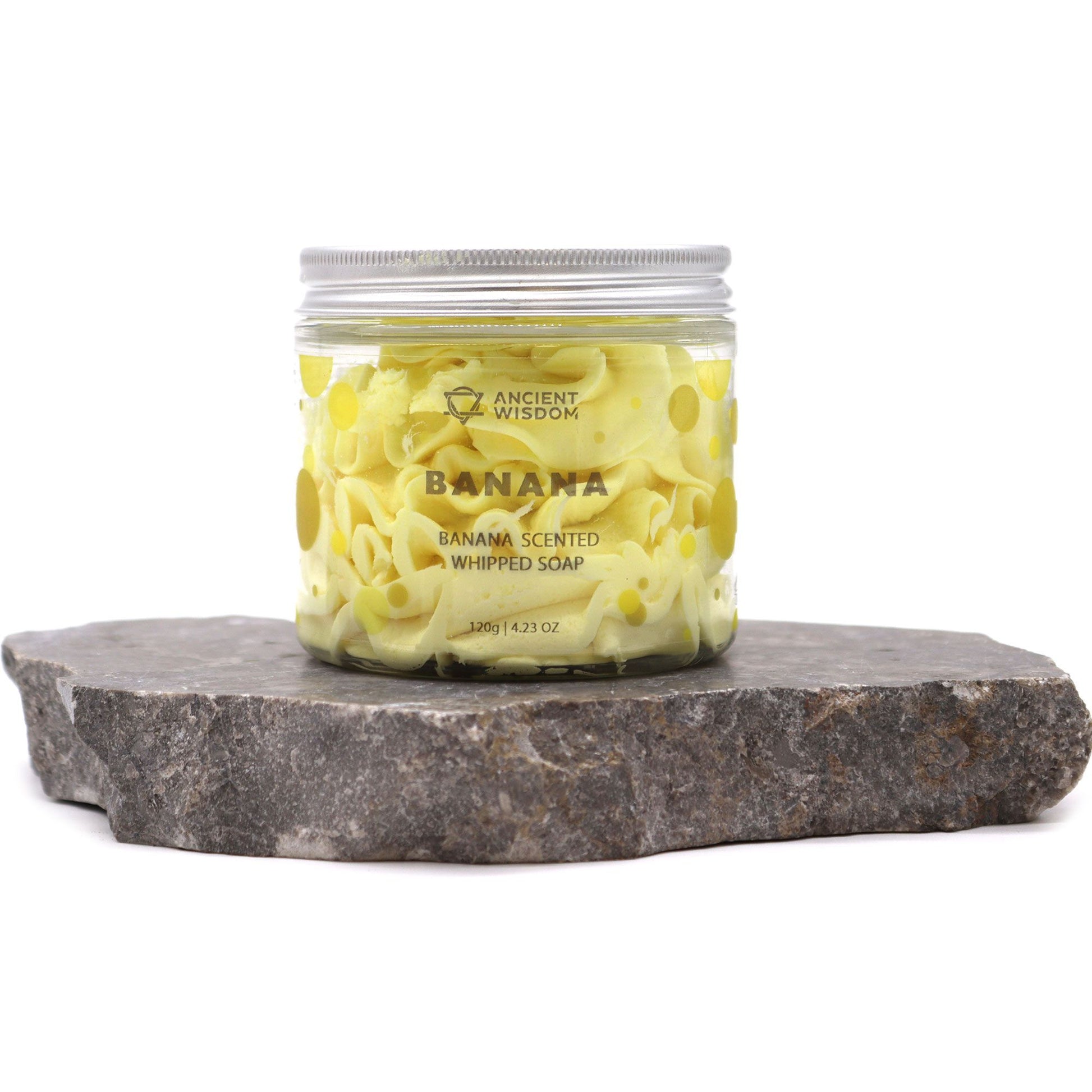 Banana scented whipped soap 120g in a clear jar with yellow banana pieces, placed on a dark stone slab.
