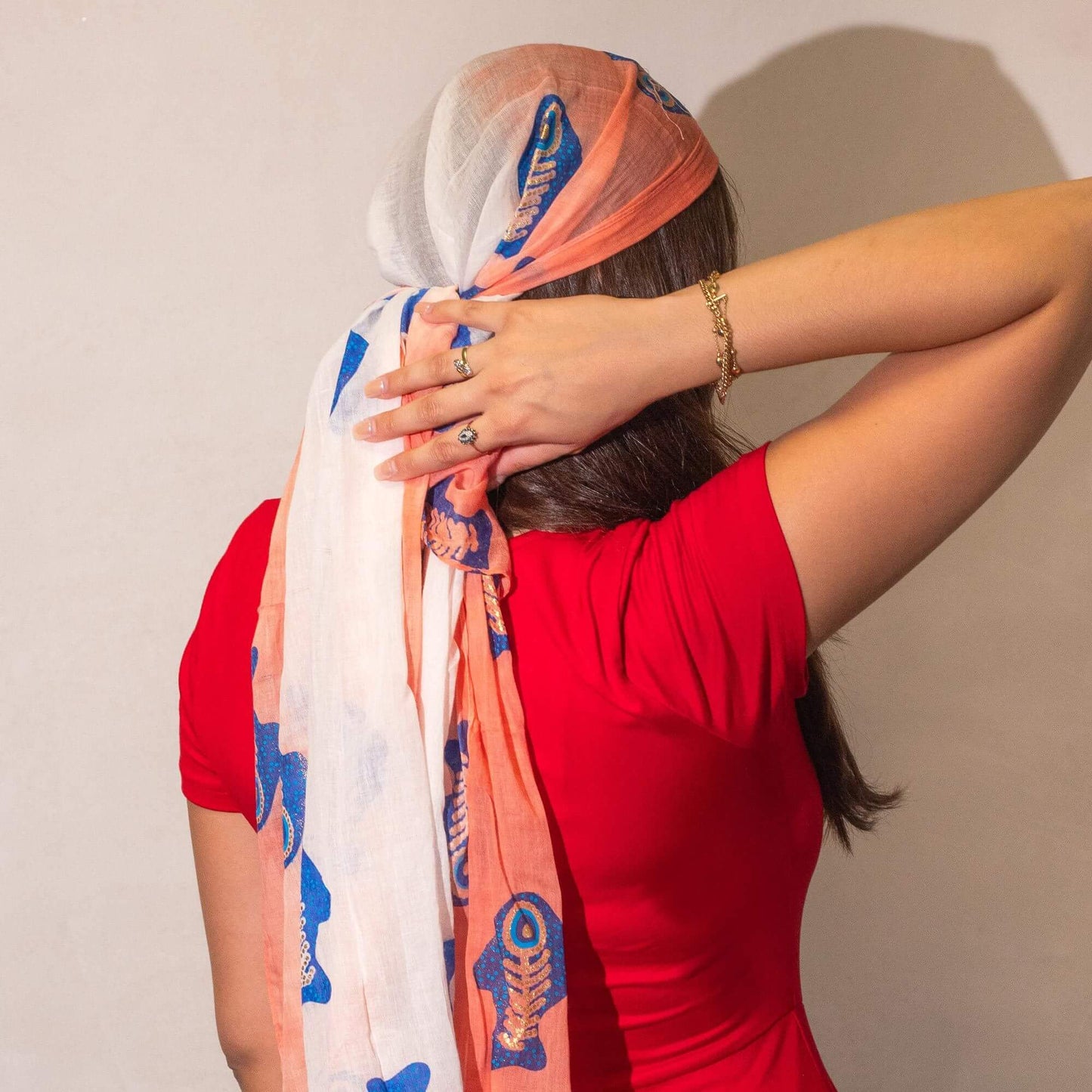 Woman wearing a colorful headscarf and red top against a plain background