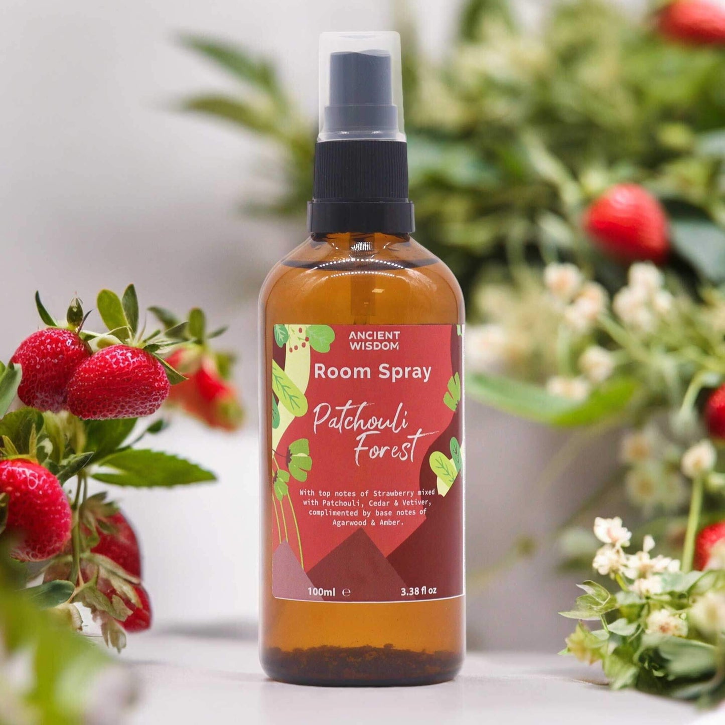 Ancient Wisdom Summer Room Spray - Patchouli Forest 100ml amber spray bottle with strawberry and floral background