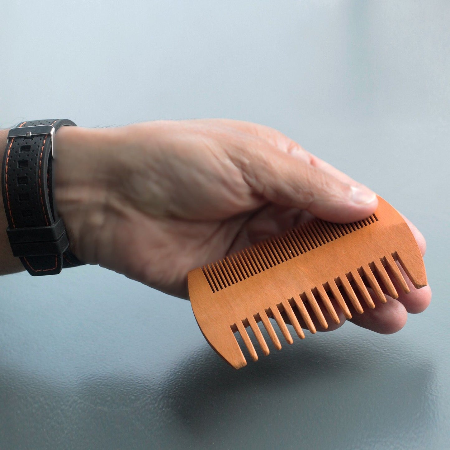 Two-sided wooden beard comb in bare wood, held in hand for precise beard grooming.