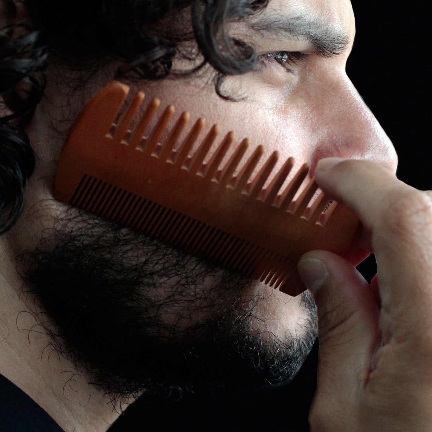 Two-Sided Beard Comb in bare wood used by a man to groom his beard.