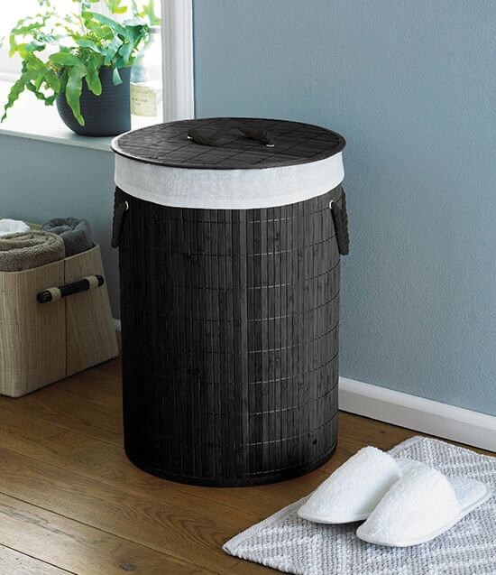 Black woven laundry basket with white liner in a room with a plant and wooden floor.