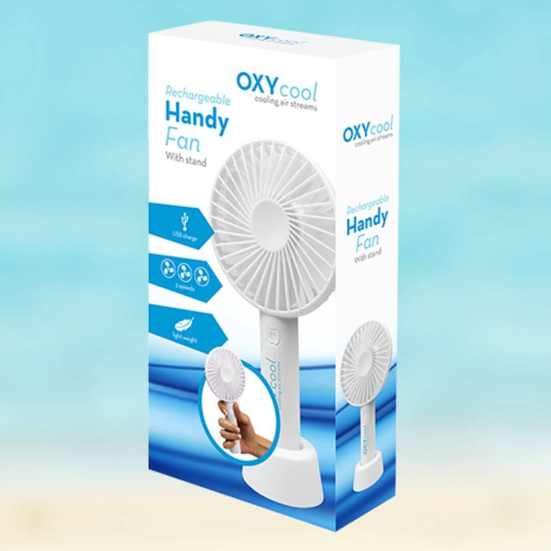 A boxed handheld fan product on a soft blue gradient background. The package is white with blue graphics and text reading 'OXYcool Handy Fan' and 'Rechargeable Handy Fan With stand,' and it shows a white portable fan pictured on the box.