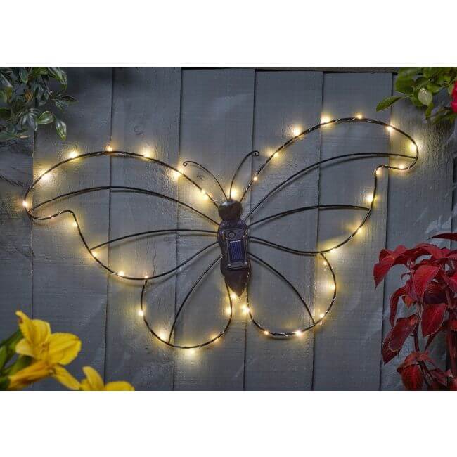 Butterfly-shaped decorative light with string lights on a wooden wall.
