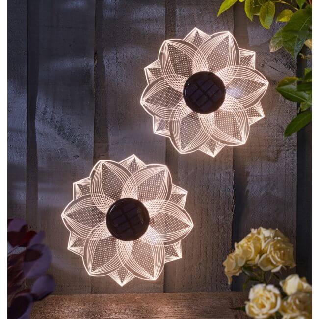 Two floral-patterned solar lights on a wooden surface with flowers in the background.