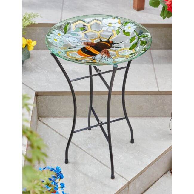 Decorative glass bird bath with floral design on a metal stand outdoors.