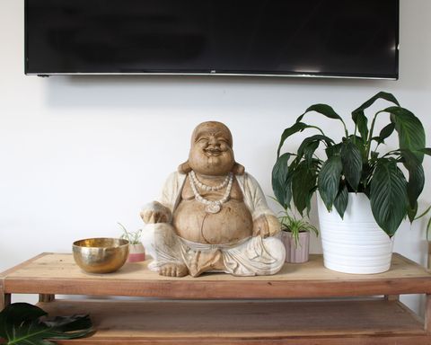Happy Buddha - Whitewash 50cm statue on a wooden table, surrounded by plants, showcasing intricate Balinese craftsmanship.