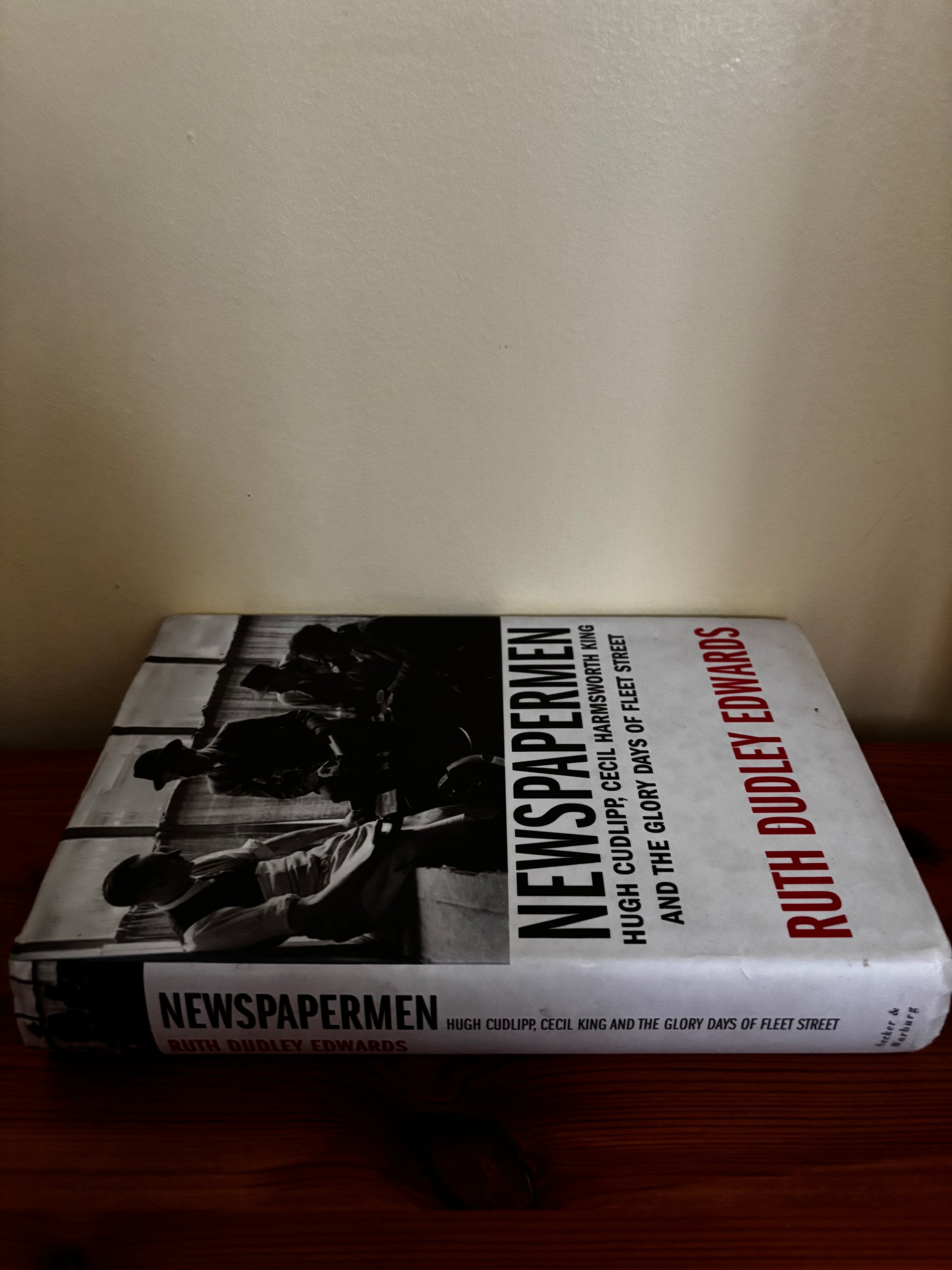 Cover of "Newspapermen: Hugh Cudlipp, Cecil Harmsworth King and the Glory" by Ruth Dudley Edwards on a wooden surface.