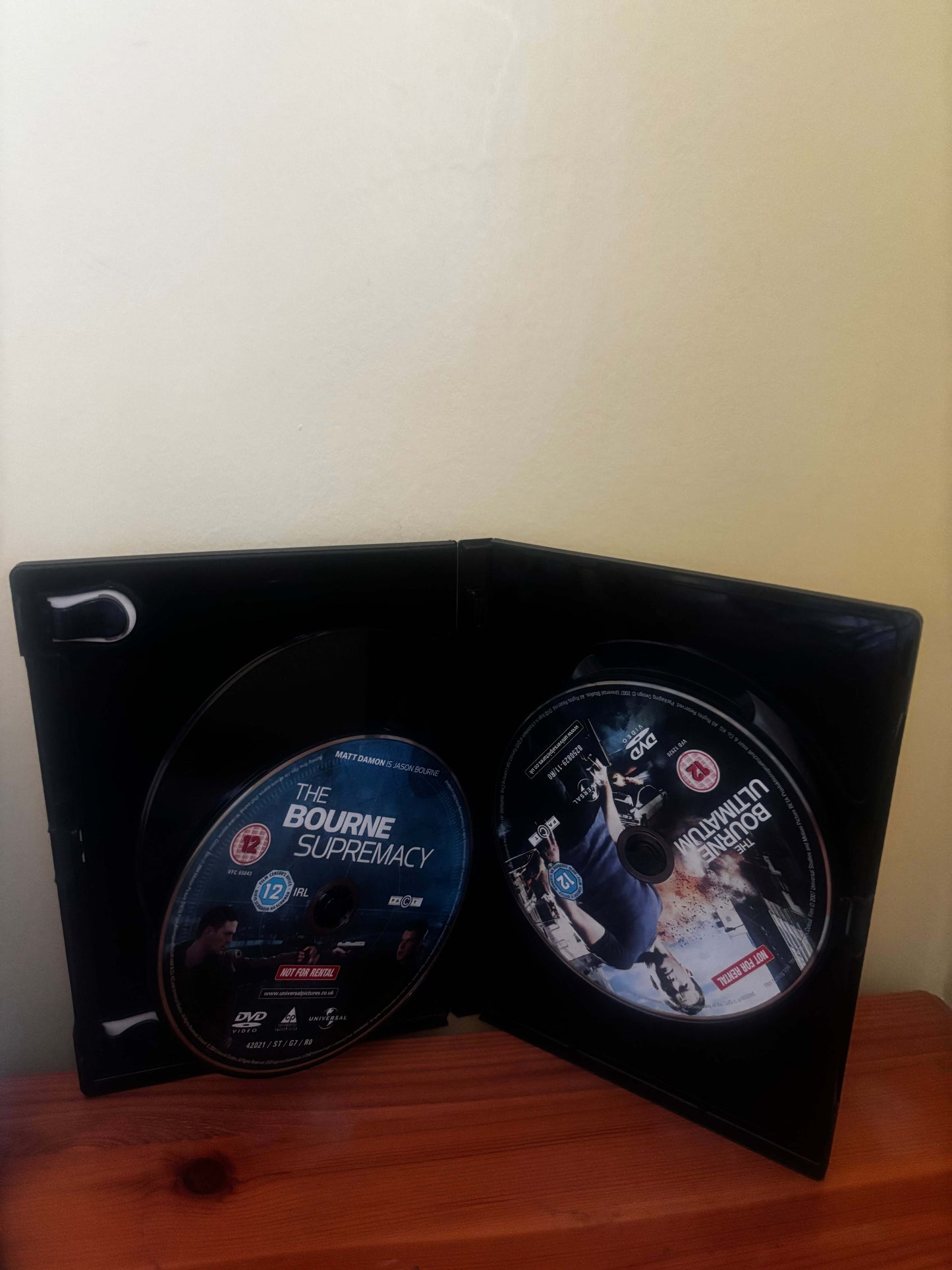 Two DVDs in a black case on a wooden surface with a white background
