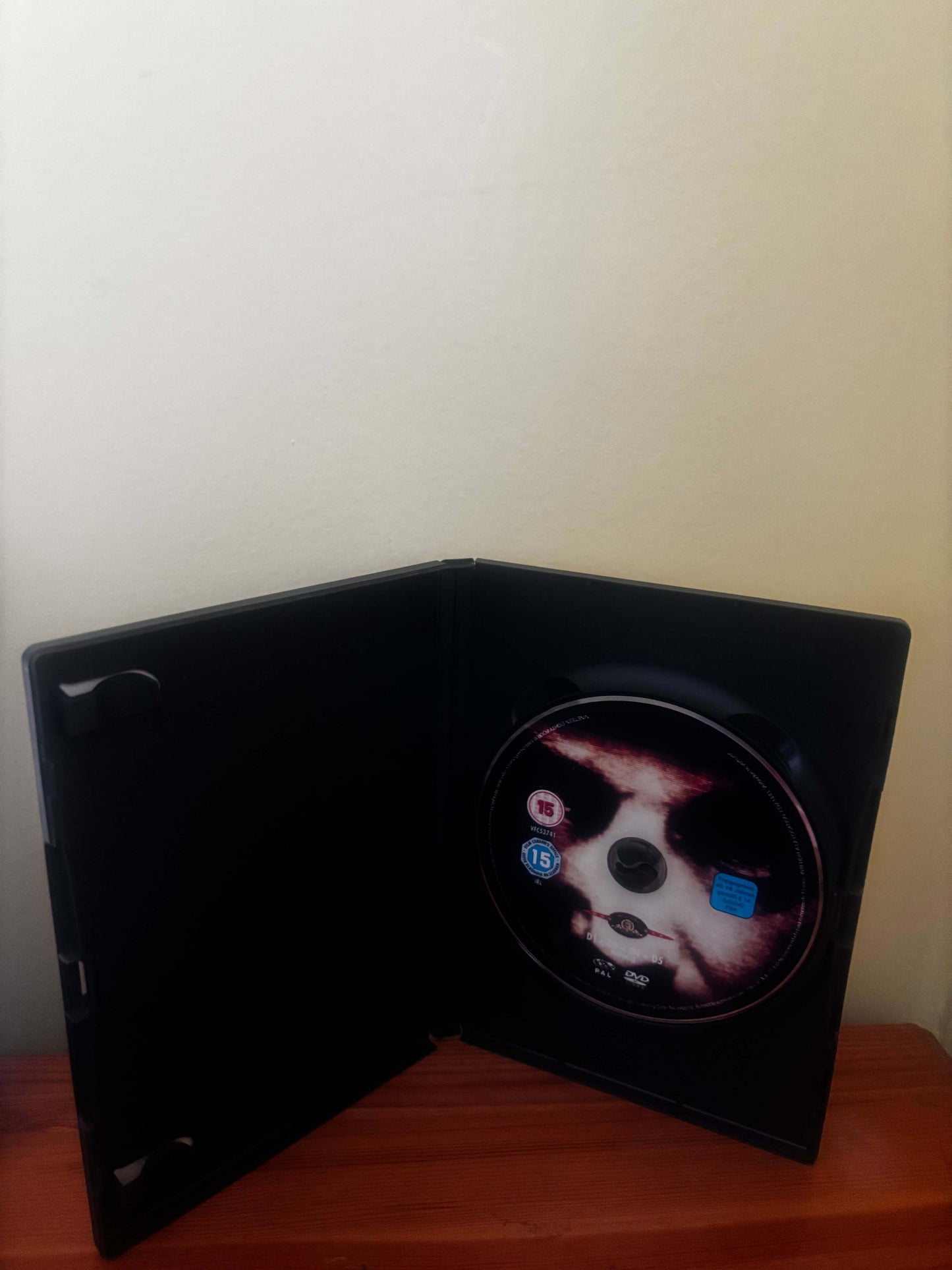 DVD case with a disc featuring a stylized face on a wooden surface.
