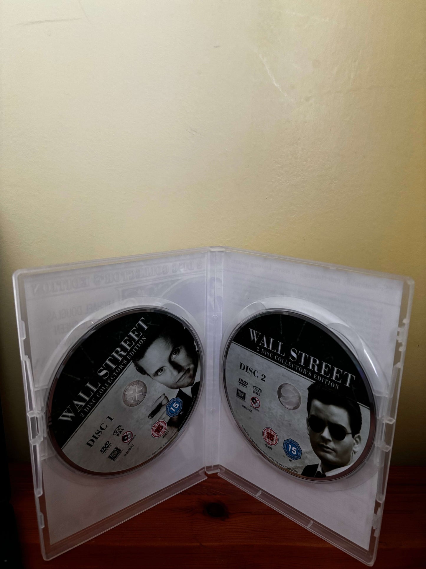 Two DVDs in a case titled 'Wall Street' on a beige surface.