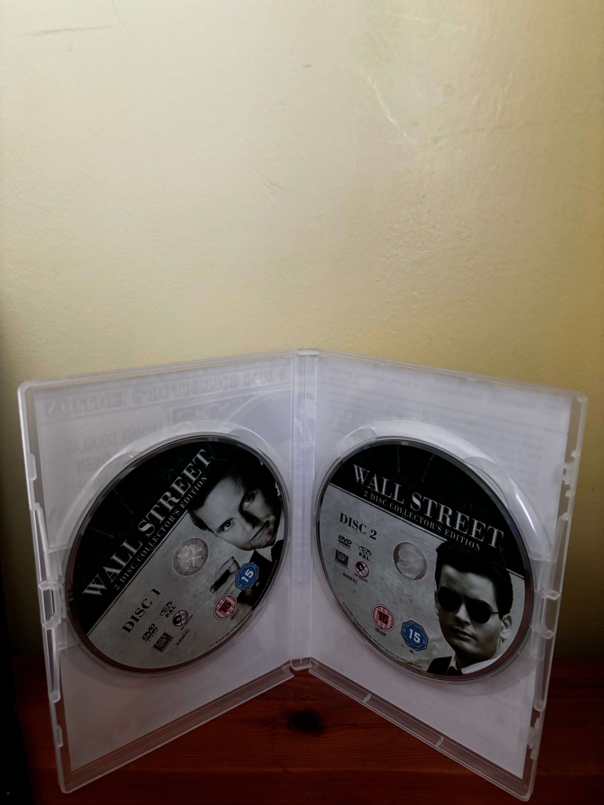 Two DVDs in a case titled 'Wall Street' on a beige surface.