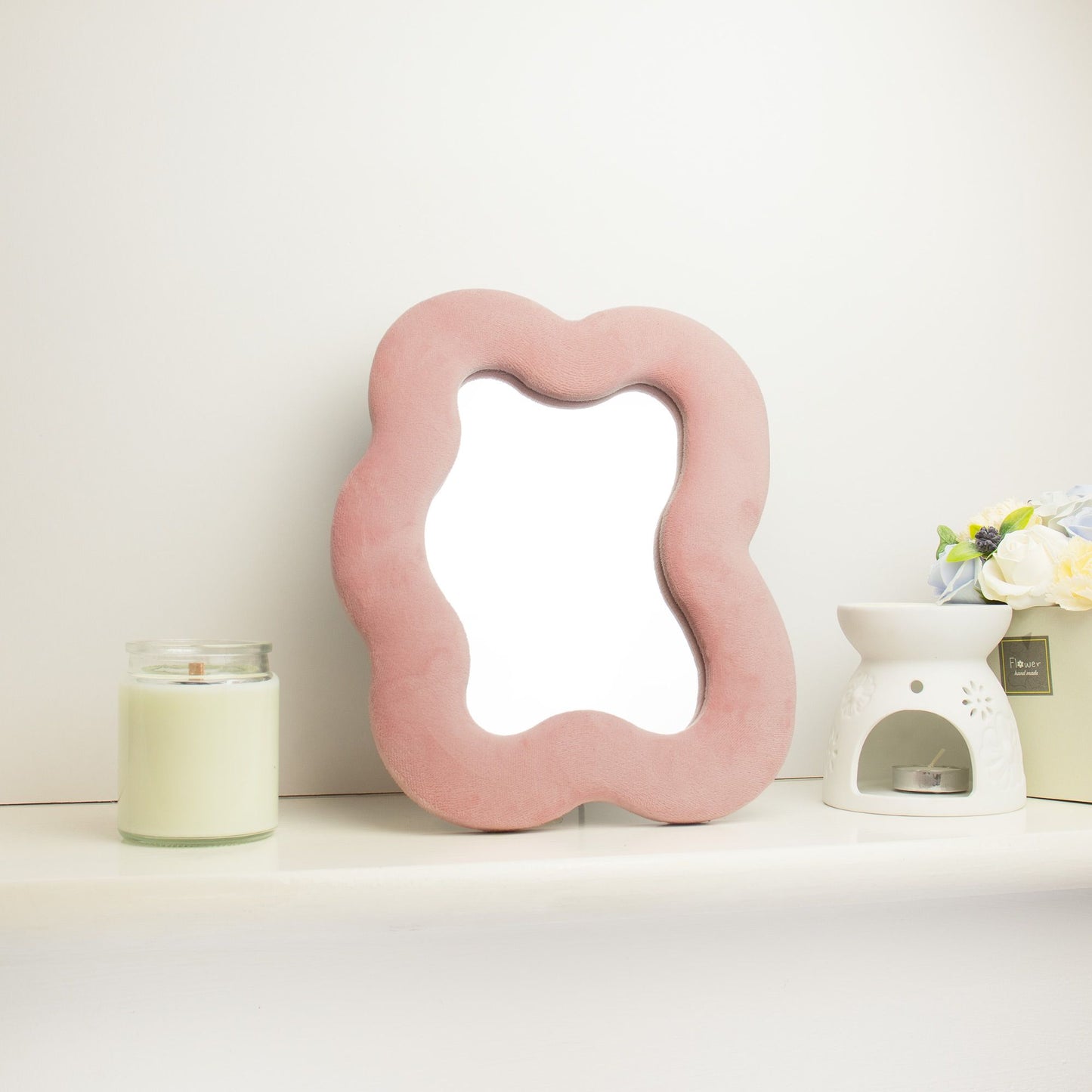 Pink cloud-shaped mirror on a white surface with a candle and small plant in the background.