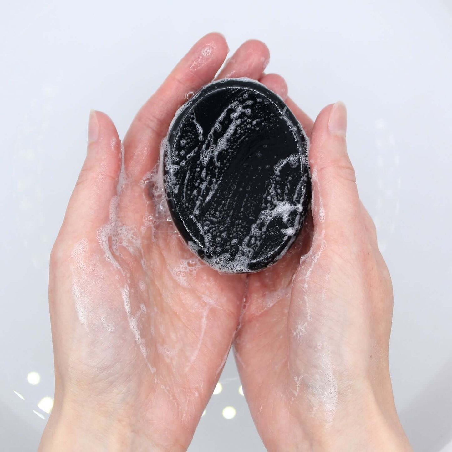 Hands washing Charcoal Soap 85g - Tea Tree with lather and bubbles, showcasing its cleansing properties.