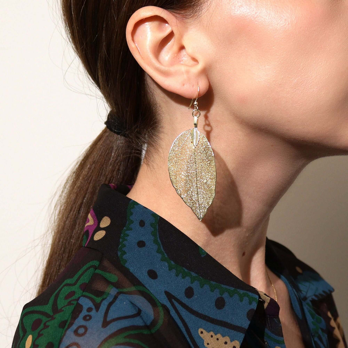 Close-up of a person wearing a silver leaf-shaped earring with a blurred background