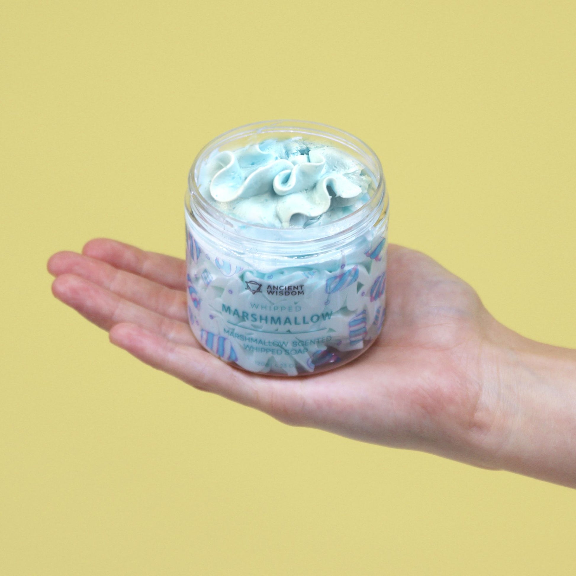 Hand holding a 120g Marshmallow Whipped Soap jar with blue swirled top.