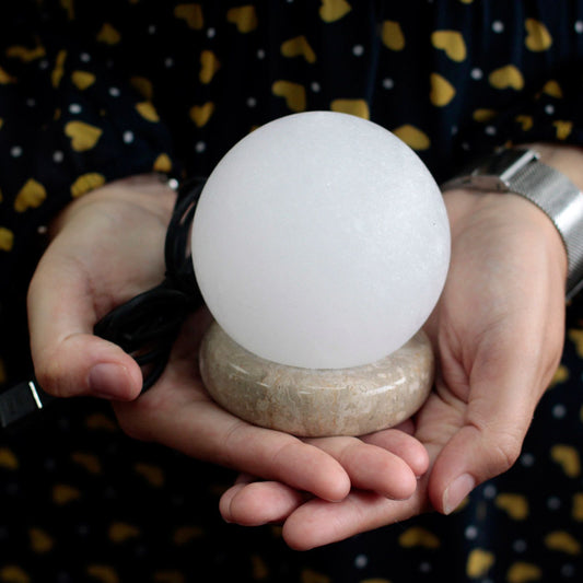 Quality USB Ball WHITE Salt Lamp - 9 cm (multi) held in hands on a stone base with USB cord.