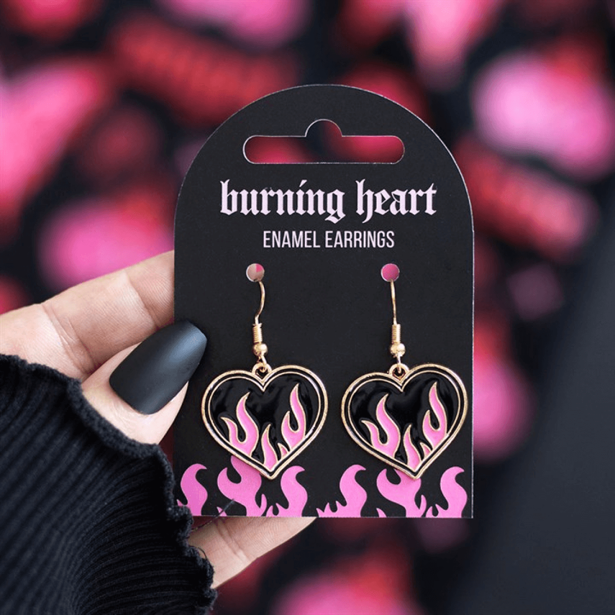 Burning Heart Earrings displayed on card with pink flames and a hand holding them, ideal for edgy statement jewellery.