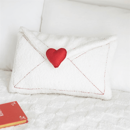 Love Letter Boucle Valentine's Day Cushion With Red Heart Envelope on a bed with a book.