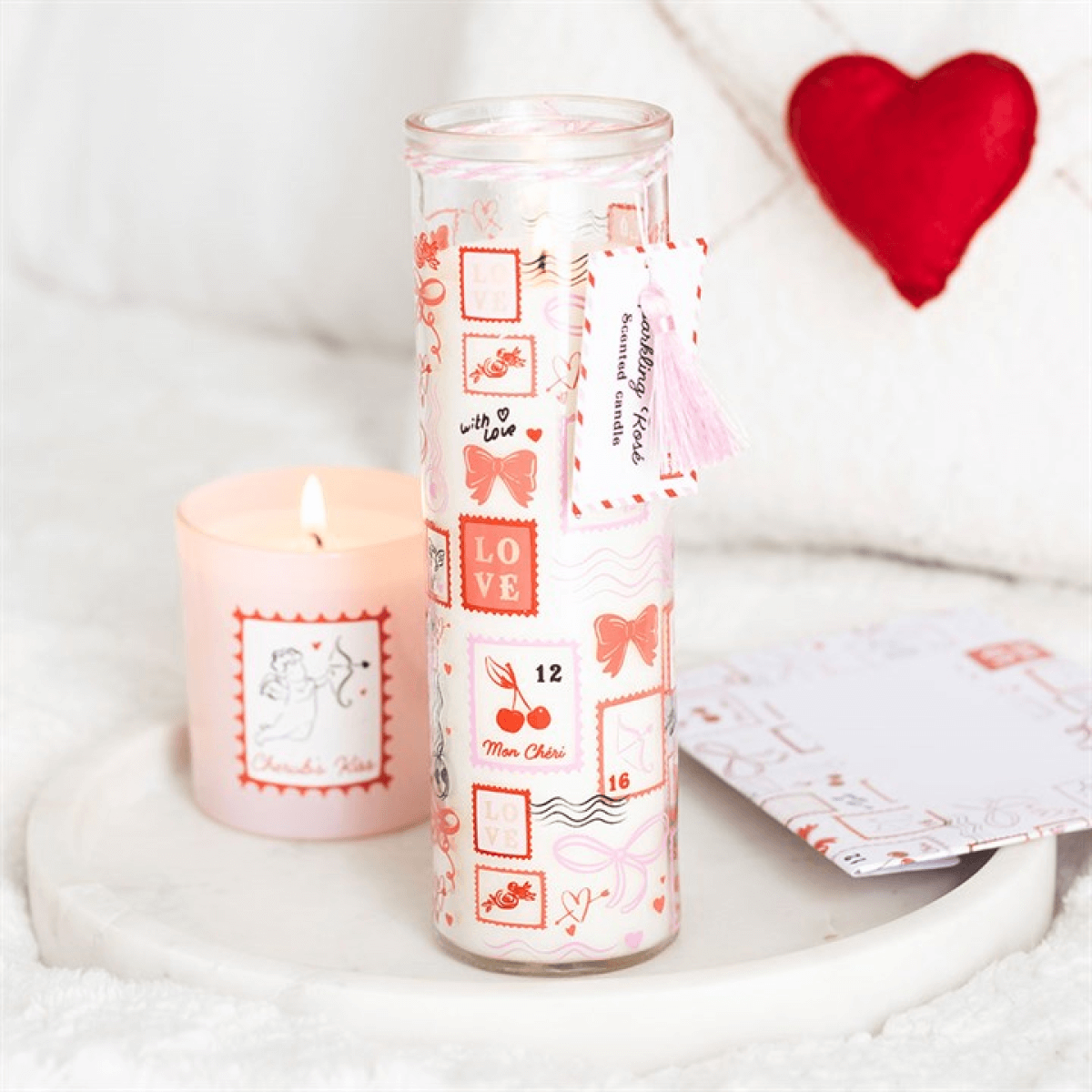 Valentine Candle in a stylish tube design with postage stamp print, next to a lit candle on a cozy surface.