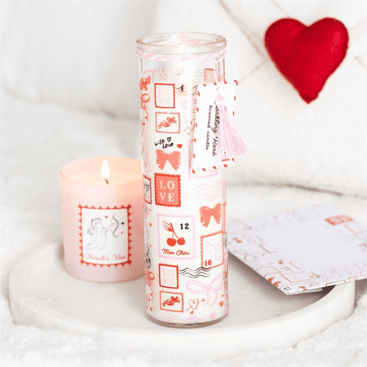 Valentine Candle in a stylish tube design with postage stamp print, next to a lit candle on a cozy surface.