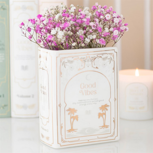 White book-shaped ceramic vase with pink and white dried flowers, a literary home décor accent.