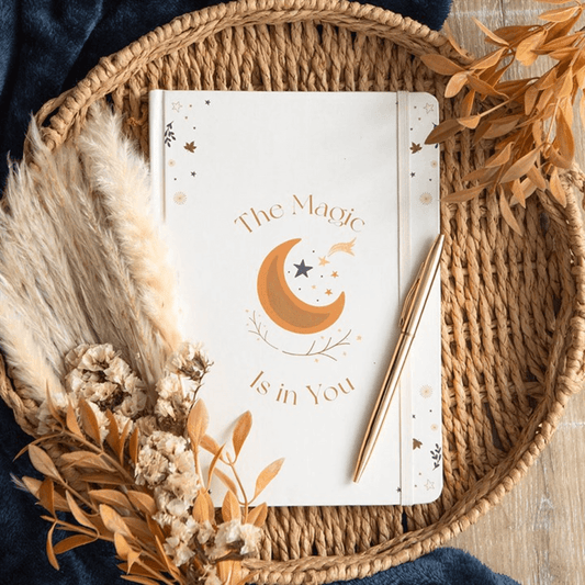 The Magic Is In You A5 Notebook for Writers Artists Dreamers placed on a woven tray with dried flowers.