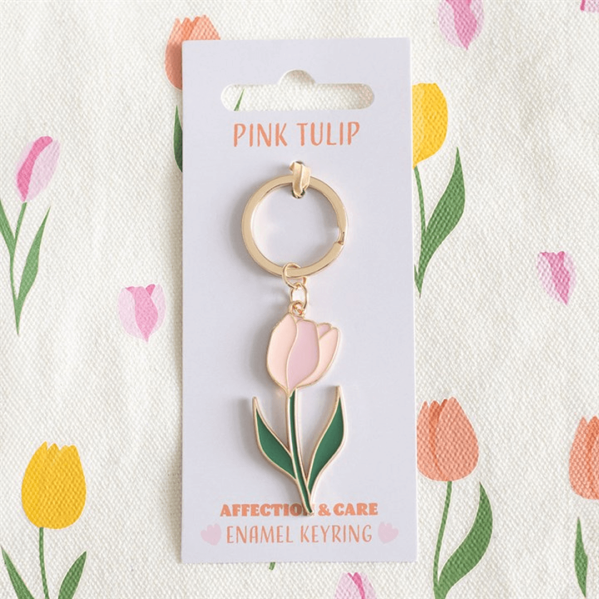 Pink Tulip Keyring on floral patterned background, featuring a charming pink tulip design with metal alloy and enamel.